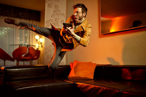 A mid-air 1970's style undercover spy or mobster sporting a leather jacket, turtleneck, gold chain and slacks, jumps over a leather couch with a pistol ready to fire.  Vintage styled room with orange lighting.  Horizontal with copy space.