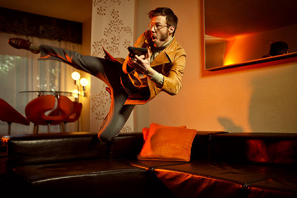 Retro Secret Agent Man Diving Over Couch A mid-air 1970's style undercover spy or mobster sporting a leather jacket, turtleneck, gold chain and slacks, jumps over a leather couch with a pistol ready to fire.  Vintage styled room with orange lighting.  Horizontal with copy space. gangster photos stock pictures, royalty-free photos & images