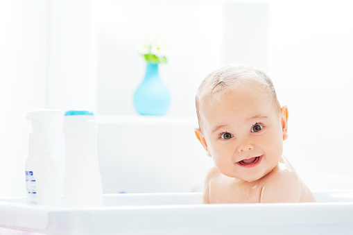 Cute Smiling Expression of beautiful baby girl 6 months old having fun in baby bath, candid, real people