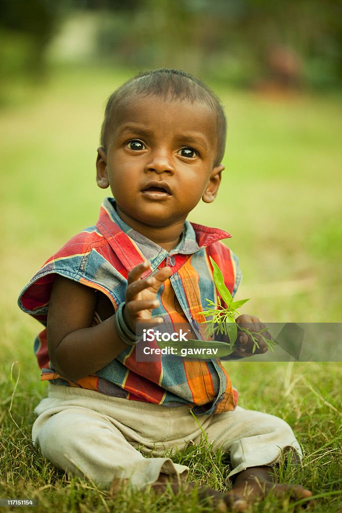 Ребенок сидит на траве, держа зеленый листья и Смотреть вверх - Стоковые фото 6-11 месяцев роялти-фри