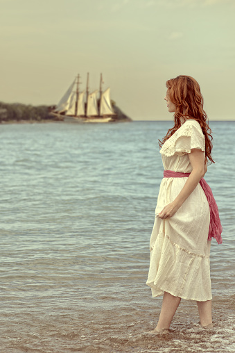 portrait of vintage style woman walking in ocean with tall ship