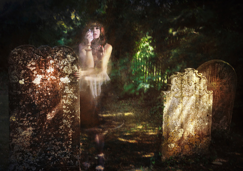 A ghostly figure of a woman cries in anguish among ancient tombstones as she appears from the background undergrowth. 