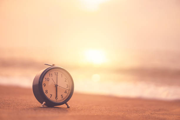istock Clock on sand beach in morning suns light with smooth wave background. 1171525006