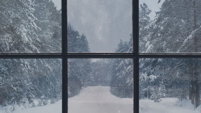 Silhouette of a wooden window overlooking the winter forest. Beautiful winter landscape with falling snow.