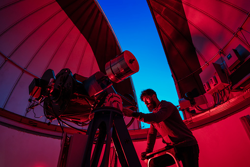 Astronomer in photo telescope dome with red light checking settings for the coming night