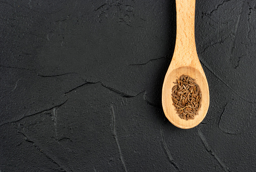 Small spoon with dry cumin close-up on concrete background