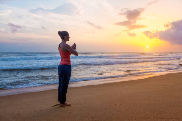 femme faisant le yoga sur la plage - salutation au soleil photos et images de collection