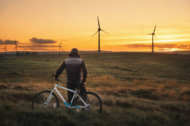 A cyclist stands in a field and looks at the windmills on the sunset stock photo