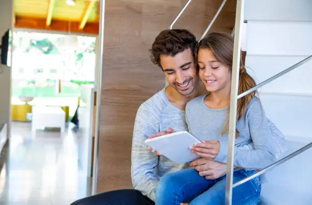 Father and daughter with tablet pc sitting in stairs at home