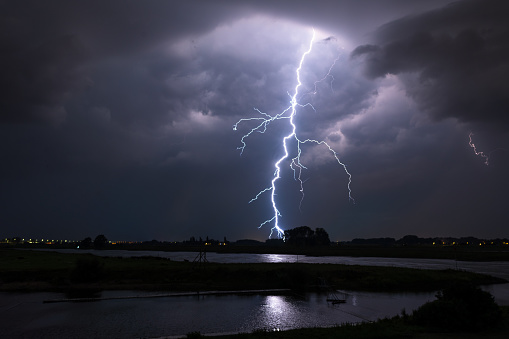 Lightning from a severe thunderstorm near a river at dusk.