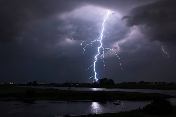 bright lightning bolt with many side branches strikes down to earth in a river landscape - flowing water flash imagens e fotografias de stock