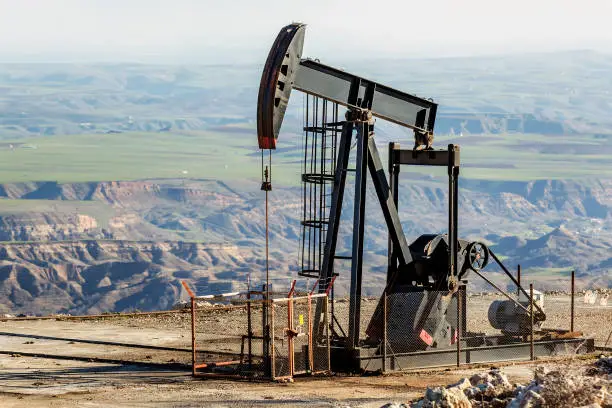 Close up view an oil pumpjack with black color in the mountain of oil rich area. It is used to mechanically lift liquid out of the well if not enough bottom hole pressure exists for the liquid to flow all the way to the surface.