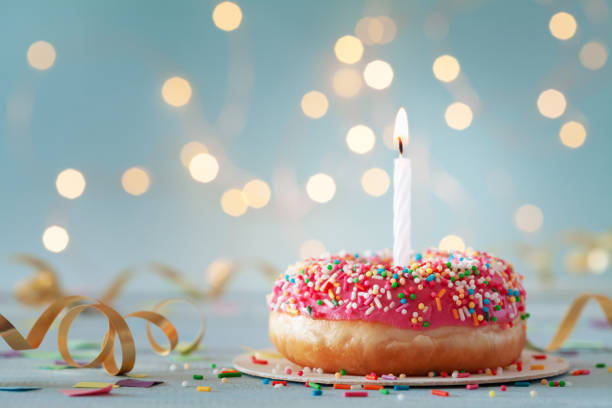 Pink donut and one burning candle against bokeh light background. Happy birthday concept. stock photo