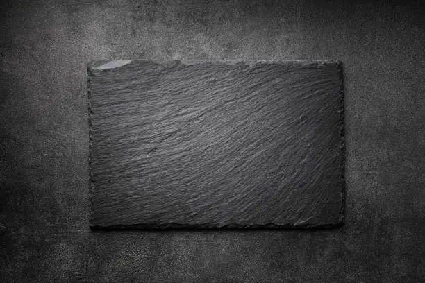 Photo of Black slate board on dark stone texture top view. Empty space for menu or recipe.