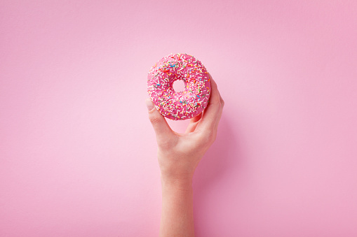 Woman hand holding pink donut or doughnut on pastel background. Flat lay style.