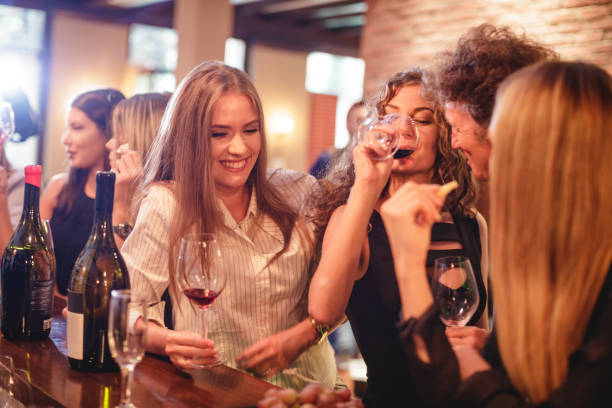 Man making young women laugh at winetasting party Mid adult man making young women laught at the winetasting party by the bar counter awful taste stock pictures, royalty-free photos & images