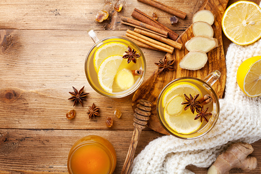 Healing ginger tea in two glass mug in scarf with lemon, honey and spices. Autumn hot drink on rustic wooden table top view with copy space.