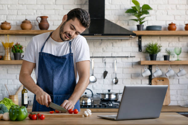 istock Handsome smiling caucasian man cooking on kitchen while talking on mobile phone with laptop on table 1171560595