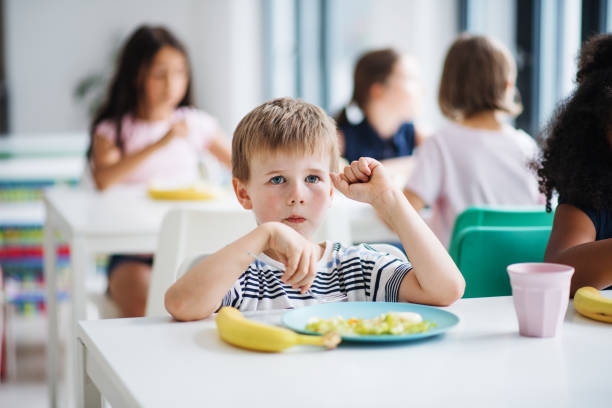 A group of cheerful small school kids in canteen, eating lunch. A group of cheerful small school kids in canteen, eating lunch and talking. food elementary student healthy eating schoolboy stock pictures, royalty-free photos & images