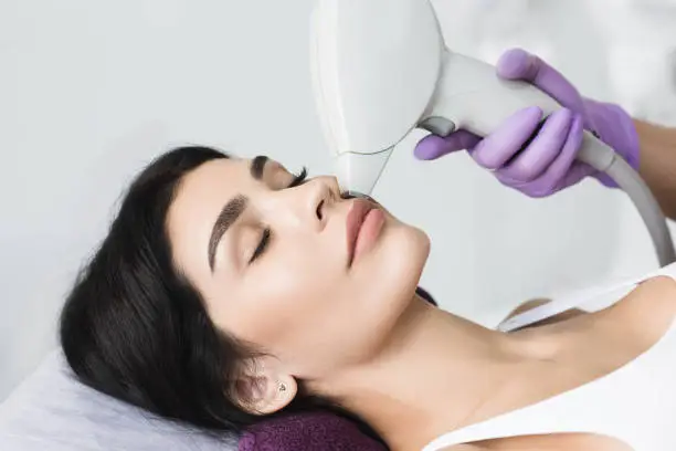 Photo of Pretty brunette woman getting hair removing on face. Procedure laser epilation at beauty studio