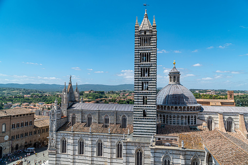 View of Siena and its white and black striped cathedral, under a slightly cloudy sky.