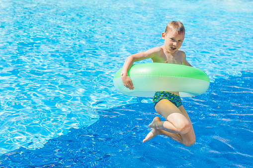 happy boy with green inflatable jumping in the pool