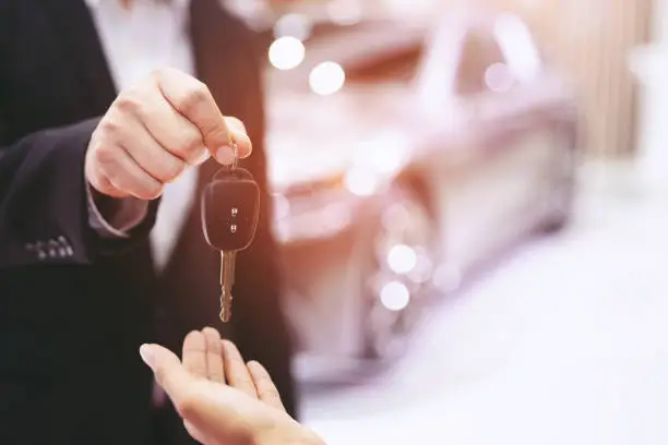 Photo of Car key, businessman handing over gives the car key to the other woman on car background.