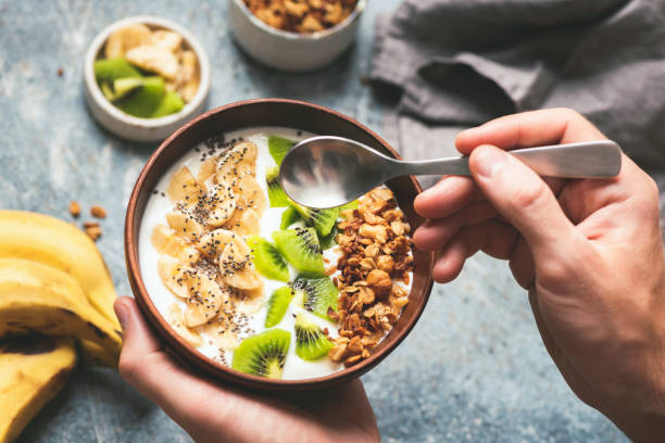 Eating healthy breakfast yogurt bowl with granola and fruits Eating healthy breakfast yogurt bowl with granola and fruits kiwi, banana, coconut. Male hands holding coconut bowl with yogurt and fruits eating chia seeds stock pictures, royalty-free photos & images