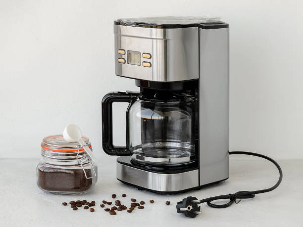 Filter holder with filter both are inside of drip-type coffee maker. Glass jug is on a plate. Ground coffee is in clip top glass jar. Coffe machine is ready for first use. Home electrical appliances. Domestic life. Front view. soporte de filtro con filtro ambos están dentro de la cafetera tipo goteo. la jarra de vidrio está en un plato. el café molido está en un frasco de vidrio clip superior. la máquina de coffe está lista para su primer uso. electrodomésticos para el ho