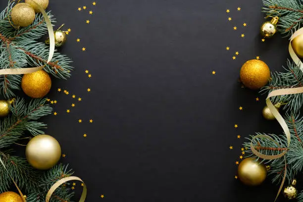 Photo of Black Christmas background with golden decorations, baubles, fir tree branches, confetti. Christmas holiday celebration, winter, New Year concept. Christmas banner mockup, greeting card template.