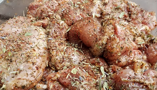 large chunks of raw chicken covered with seasonings and herbs