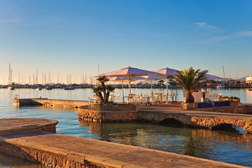 Stone pier with tables and umbrellas cafe in early morning in Port de Pollenca, Mallorca, Balearic islands, Spain