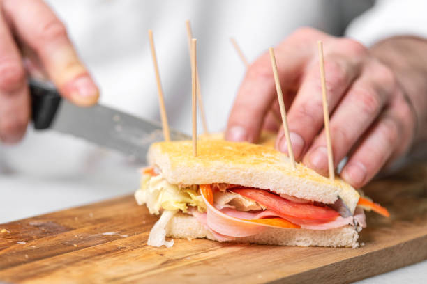 istock Chef finalizes the sandwich with ham and salad on the wooden board. 1171608041