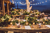 Table setting at night wedding ceremony. Decoration with fresh flowers, candles, light bulbs, garlands. VIntage style.