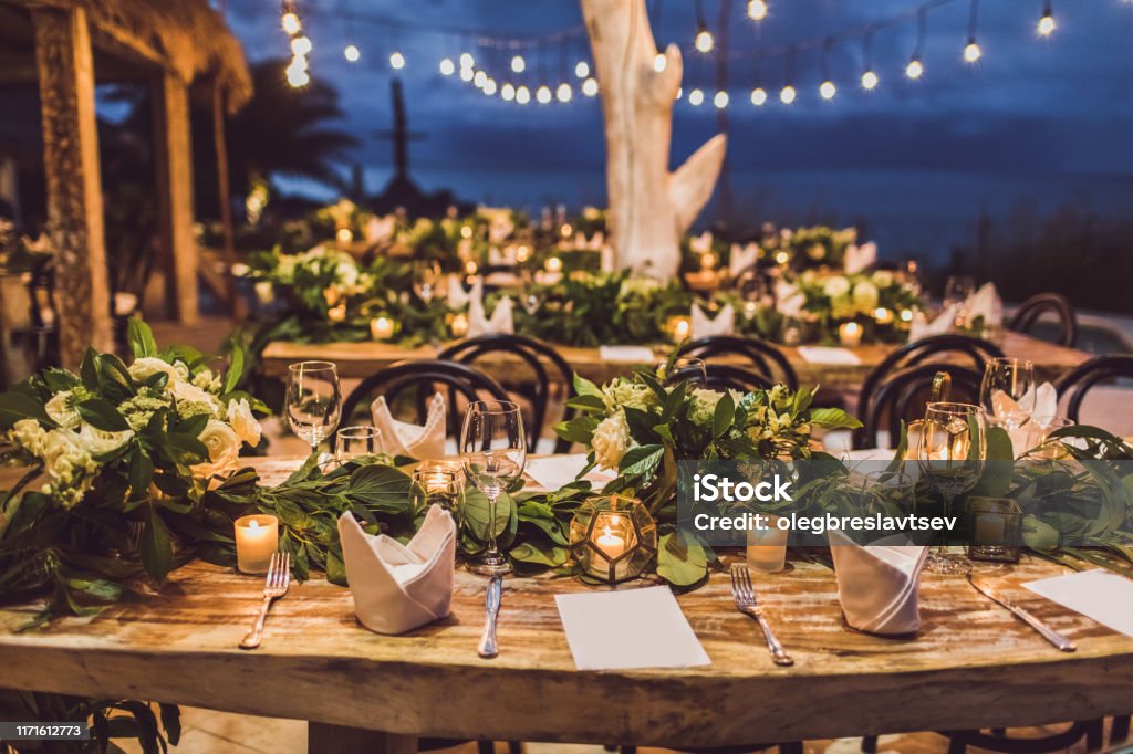 Table setting at night wedding ceremony. Decoration with fresh flowers, candles, light bulbs, garlands. VIntage style. Outdoors Stock Photo