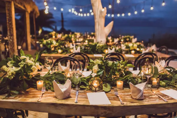 Photo of Table setting at night wedding ceremony. Decoration with fresh flowers, candles, light bulbs, garlands. VIntage style.