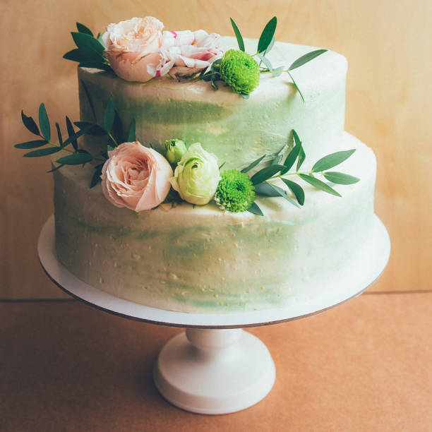 istock Three-tiered white wedding cake decorated with flowers from mastic on a white wooden table. Picture for a menu or a confectionery catalog with copy space. 1171612794