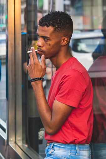 Photo of an afro decendent guy, smoking at a urban street