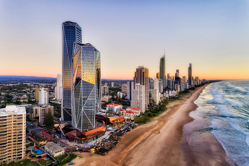 Reflecting facets of modern urban high-rise towers on Australian Gold Coast in Queensland - Surfers Paradise. Wide sandy long beach of Pacific shore at sunrise in elevated aerial view along waterfront.