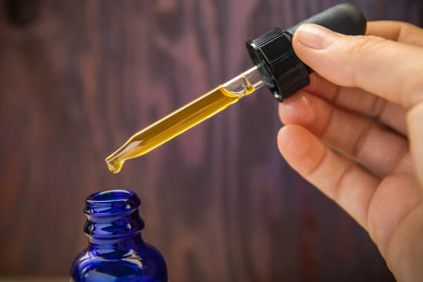 CBD Oil Extract In Dropper & Blue Bottle Up Close A dose of CBD (Cannabidiol) oil measured out of blue bottle with dropper on wooden background glass medicine blue bottle stock pictures, royalty-free photos & images