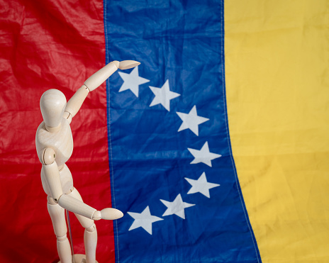 Wooden figurine carrying Venezuelan flag on white background ideal for political conflicts in Venezuela and South America. 7 stars flag
