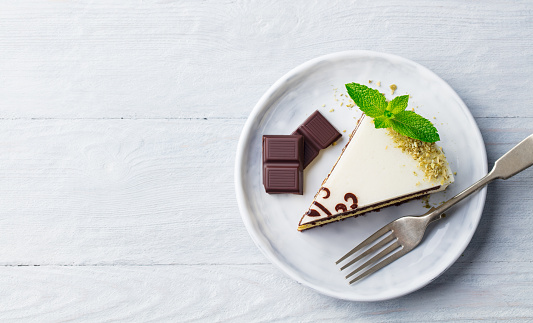 White chocolate cake with fresh mint leaf on a plate. Wooden background. Top view. Copy space
