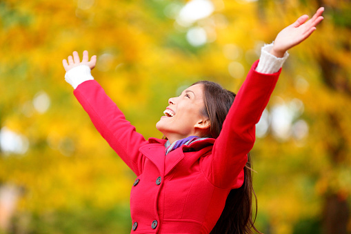 Autumn / fall woman happy in free freedom pose with arms raised up towards the sky with smiling cheerful  elated expression of happiness. Beautiful girl in colorful forest foliage outdoor.