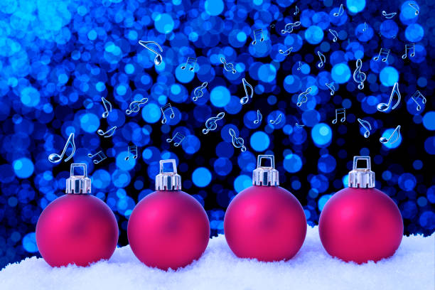 Four red Christmas ornaments on the snow, and lots of flying musical note against defocused blue Christmas lights.