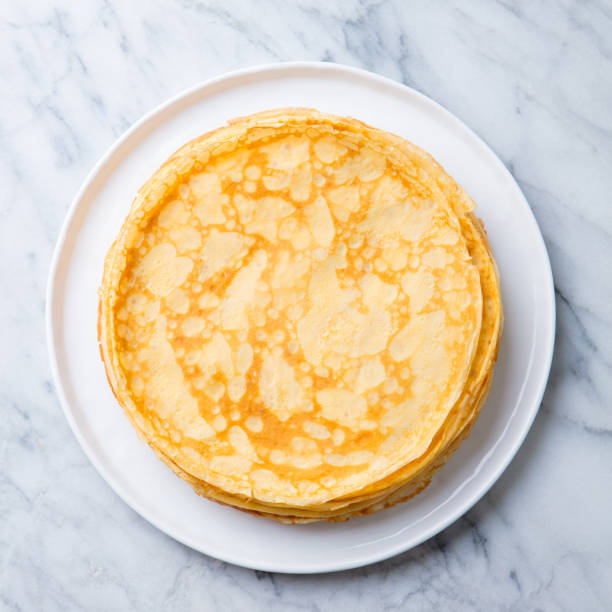 Crepes, thin pancakes on a white plate. Marble background. Copy space. Top view. stock photo