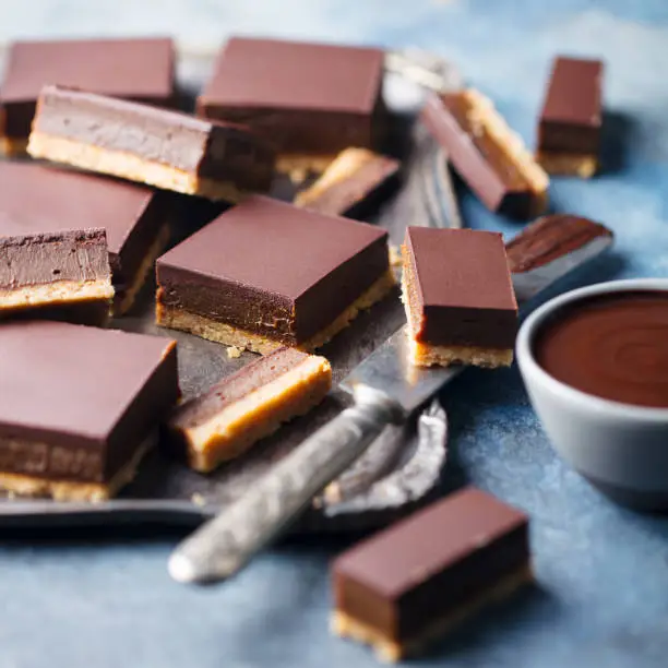 Photo of Chocolate caramel slices, bars, millionaires shortbread on a metal tray. Blue background. Close up.