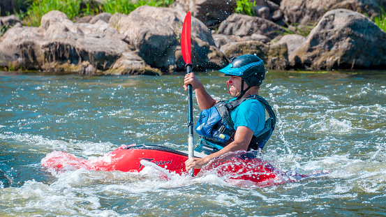 Myhiya, Ukraine - August 17, 2019: Playboating. A man sitting in a kayak with oars in his hands performs exercises on the water. Kayaking freestyle on whitewater.