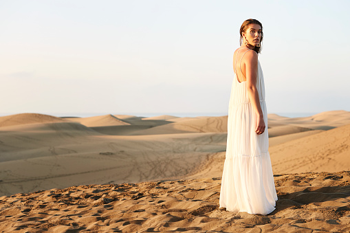 Beautiful brunette on sand dune in white dress, portrait