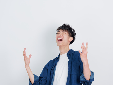 Portrait of a handsome Chinese young man in blue shirt shouting with two arms open, smiling and happy expression, isolated on white background.