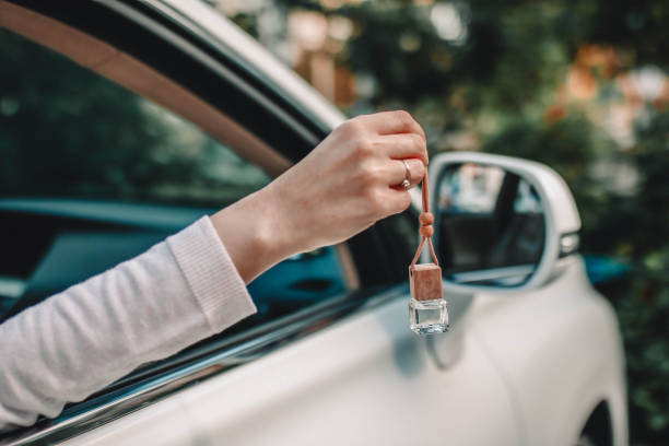 botella pequeña de vidrio con perfume de coche en mano femenina. pequeña botella de vidrio con perfume de coche colgando cerca del coche. - car freshner fotografías e imágenes de stock